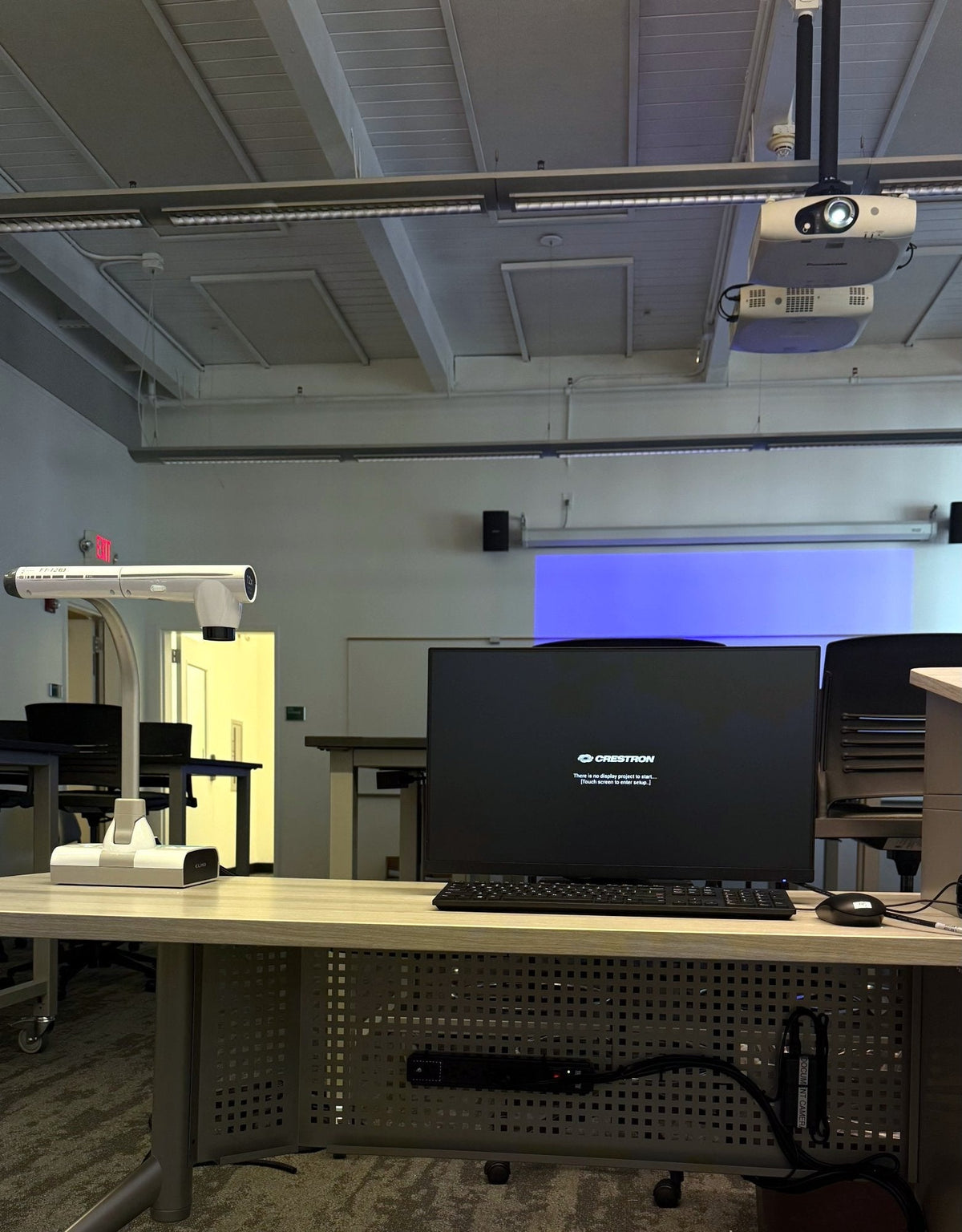 Instructor desk in a Diablo Valley College ATC classroom in Pleasant Hill, with a Planar PLN2501 monitor, a ceiling-mounted projector and Bose DM5SE loudspeakers either side of the projection screen.