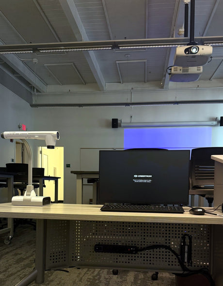 Instructor desk in a Diablo Valley College ATC classroom in Pleasant Hill, with a Planar PLN2501 monitor, a ceiling-mounted projector and Bose DM5SE loudspeakers either side of the projection screen.