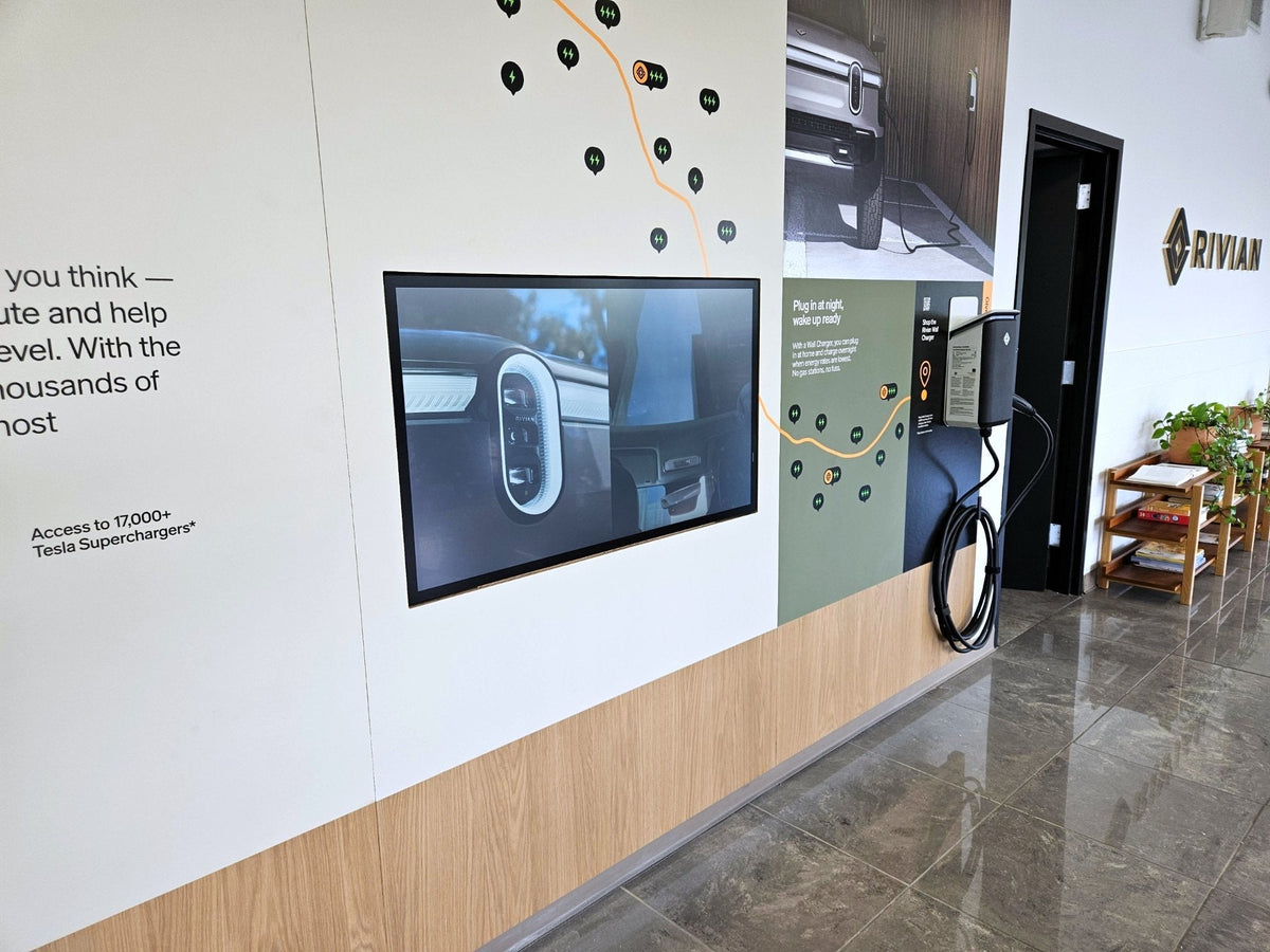 The Electric Adventure wall panel at Rivian's Franklin, Tennessee showroom, with a 43-inch Planar SLP43-T touch display flush-mounted in the graphic wall beside a Rivian wall charger.