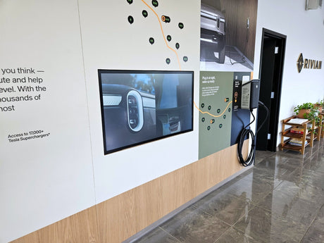 The Electric Adventure wall panel at Rivian's Franklin, Tennessee showroom, with a 43-inch Planar SLP43-T touch display flush-mounted in the graphic wall beside a Rivian wall charger.