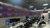 Twenty Sony FW65BZ40L displays in a two-row control room video wall with a tilted top row and QSC AD-S8T loudspeakers above, facing operator consoles in the Netflix Live Command Center in Los Gatos, California.