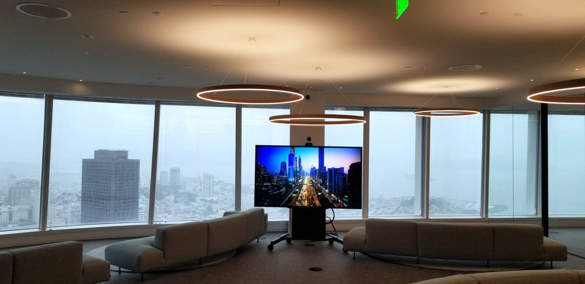 The Sky Lounge on Mubadala's 55th floor in Salesforce Tower, San Francisco, with a large-format display and PTZ camera on a Chief mobile cart in front of the curved window wall.
