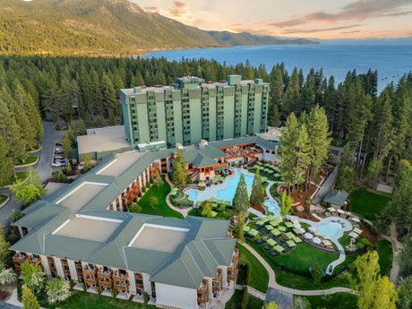 Aerial view of a hotel complex near a lake surrounded by trees.