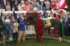 Horse adorned with a floral wreath surrounded by celebratory crowd.
