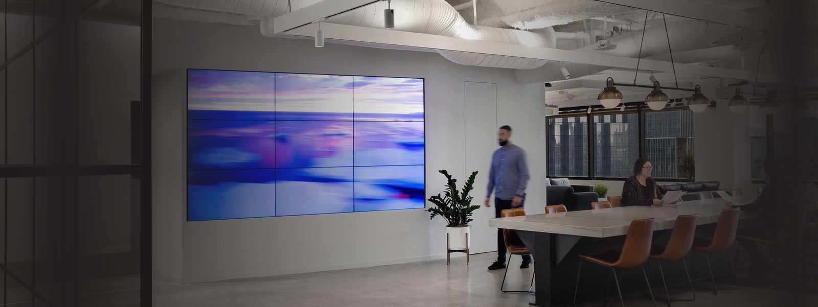 A modern office with a large screen and two people at a table.